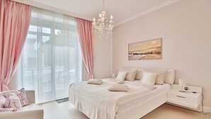 Une chambre à coucher avec un grand lit, une table de chevet, une commode, un lustre et une fenêtre avec des rideaux.