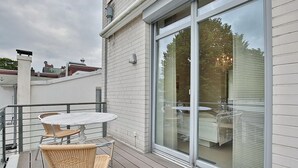 Un balcon avec une table et des chaises, une porte-fenêtre coulissante et une vue sur une maison dotée d’un balcon.
