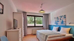 A bedroom with a bed, a desk, a chair, a window with curtains, and a painting on the wall. - Strandkoje Kastanienallee (Timmendorfer Strand)