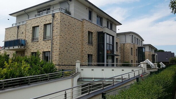 Um edifício residencial moderno de vários andares, com fachada de tijolos, janelas amplas e uma varanda.