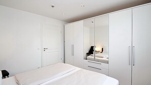 Ein Schlafzimmer mit Bett, Kleiderschrank und Spiegel, der einen Sessel und eine Lampe zeigt.