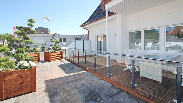 Ein modernes Gebäude mit einer Holzterrasse, Sitzgelegenheiten im Freien und Blick auf das Meer.
