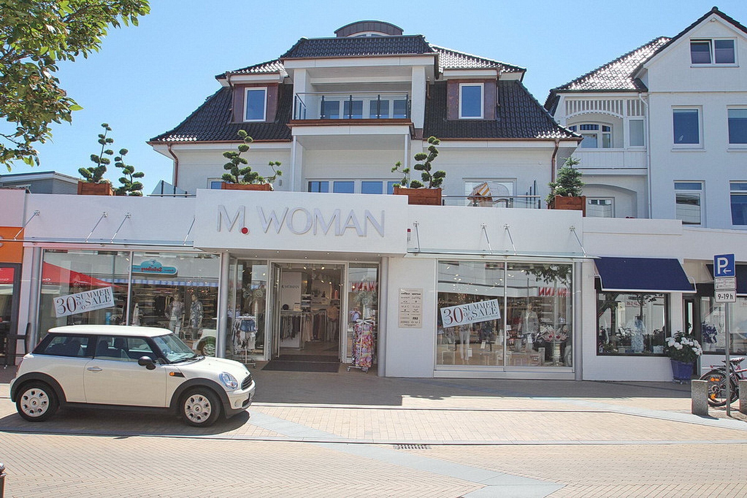 A building with a storefront labeled "M. WOMAN" and a sign indicating a 30% summer sale.