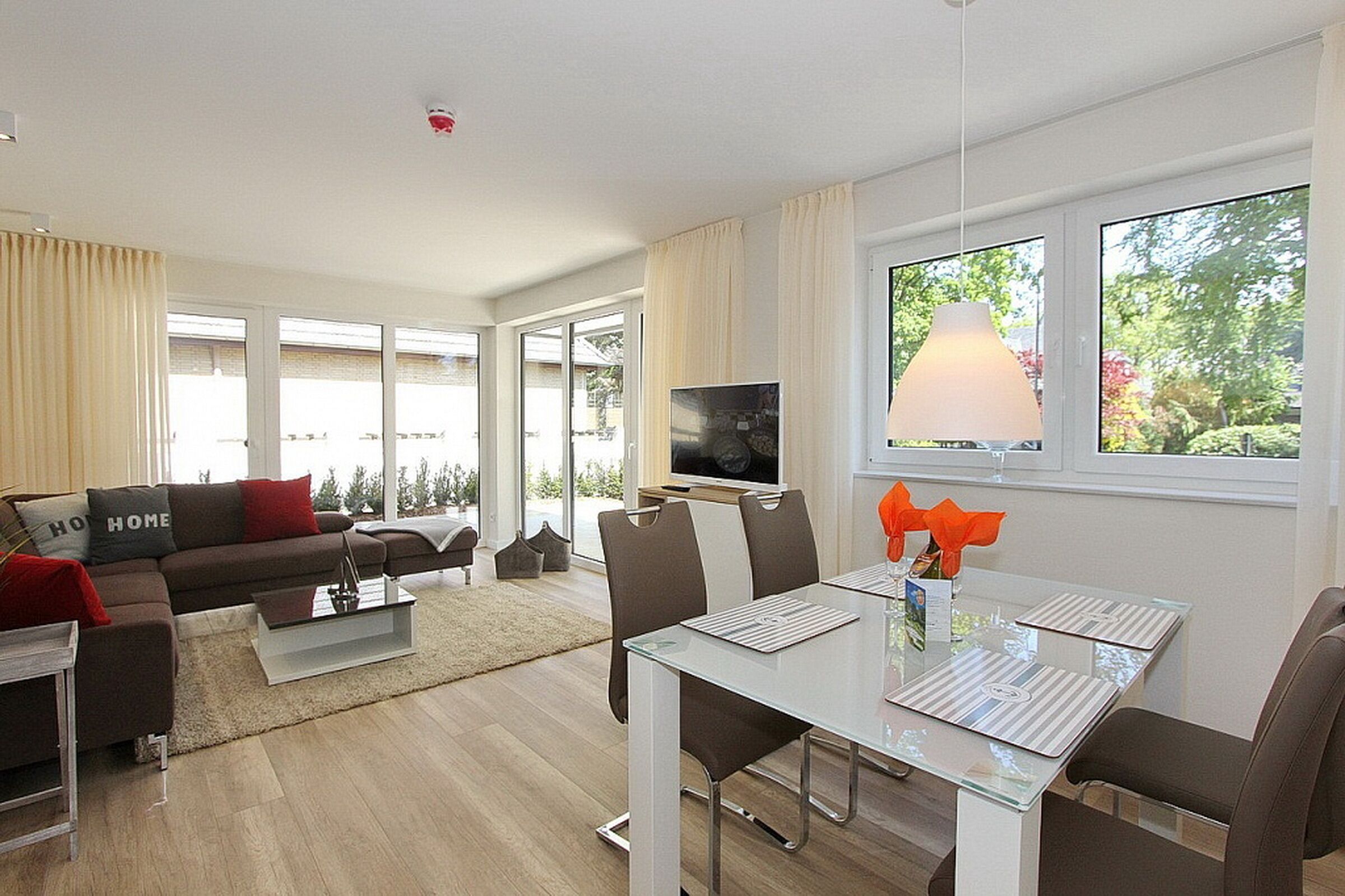 A modern living room with a sofa, TV, dining table, and large windows.