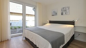Une chambre avec un lit, une porte-fenêtre coulissante donnant sur un balcon et deux œuvres d’art accrochées au mur.