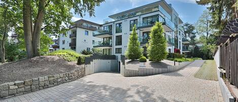 A modern multi-story building with a paved courtyard, surrounded by trees and a stone wall.