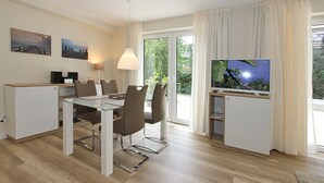 Ein modernes Wohnzimmer mit Essbereich, einem Flachbildfernseher und einem großen Fenster mit Vorhängen.