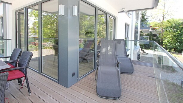 Une terrasse extérieure moderne avec des portes vitrées, des meubles en osier et un plancher en bois.