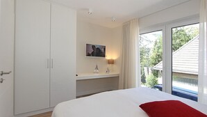 Une chambre à coucher comprenant un lit, une armoire, un bureau avec une lampe, un tableau et une fenêtre avec des rideaux.