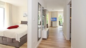 A modern hotel room with a bed, a television, a mirror, and a view of the outdoors. - Villa Stern Appartement 7 (Timmendorfer Strand)