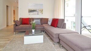 A modern living room with a sectional sofa, a coffee table, and a large window with curtains. - Villa Stern Appartement 7 (Timmendorfer Strand)