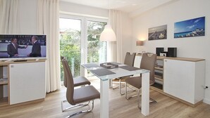 A modern room with a glass dining table, comfortable chairs, a television, and a balcony with curtains. - Villa Stern Appartement 7 (Timmendorfer Strand)