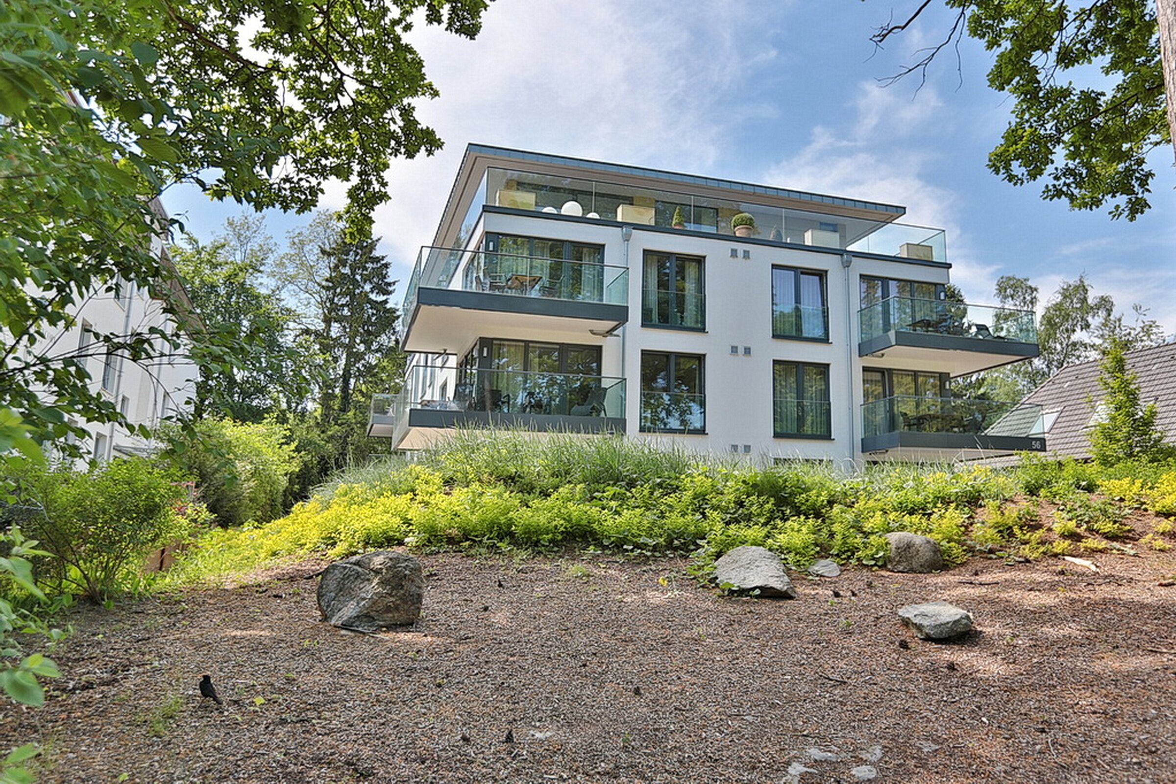 Une maison moderne à deux étages, dotée d’un balcon et entourée de verdure et de rochers.