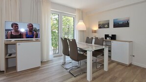 A modern, well-lit room with a dining table, chairs, a television, and artwork on the walls. - Villa Stern Appartement 9 (Timmendorfer Strand)