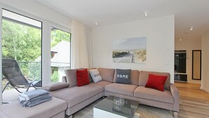 A modern living room with a sectional sofa, a glass coffee table, and a view of the outdoors through large windows. - Villa Stern Appartement 12 (Timmendorfer Strand)