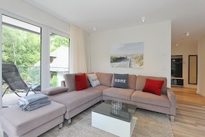 A modern living room with a sectional sofa, a glass coffee table, and a view of the outdoors through large windows.
