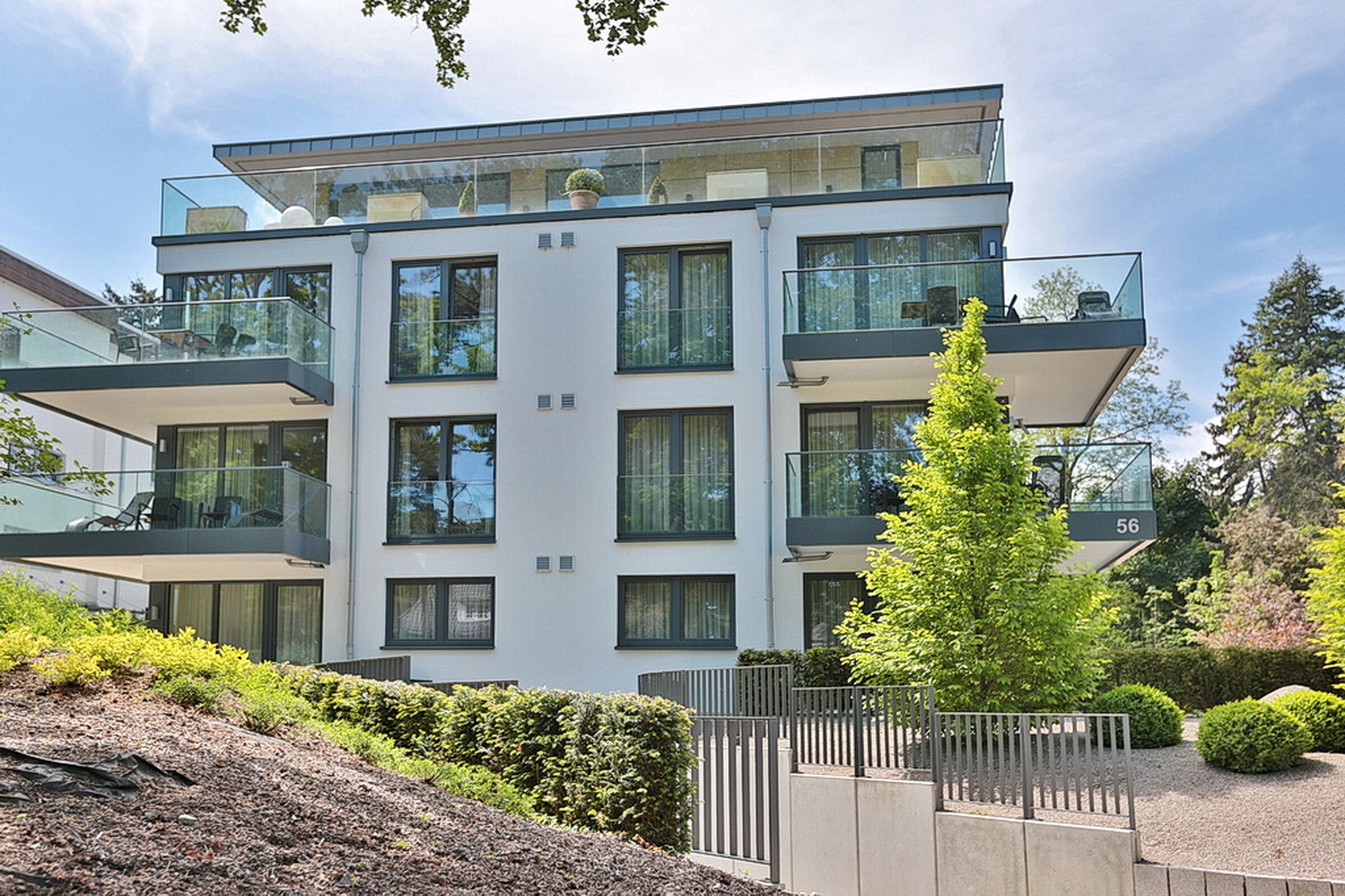 Un immeuble résidentiel moderne à plusieurs étages, doté de balcons, d’un jardin bien entretenu et offrant une vue sur un ciel dégagé.