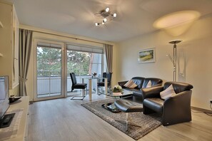A modern living room with a glass coffee table, leather sofa, and a dining area with a glass table and chairs. - Kurparkresidenz-timmendorfer Strand Appartement 27 (Timmendorfer Strand)