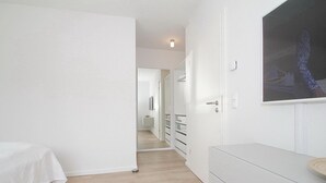 A modern, minimalist bedroom with a bed, a white dresser, and a large mirror. - Ferienanlage Bergstrasse 6 Appartement 7 (Timmendorfer Strand)