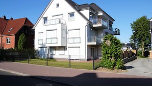 A modern two-story residential building with a balcony on the upper floor, a fenced yard, and a clear sky. - Ferienanlage Bergstrasse 6 Appartement 7 (Timmendorfer Strand)