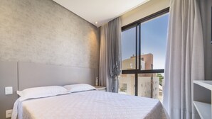 Een moderne hotelkamer met een groot bed, grijze gordijnen en uitzicht op gebouwen.