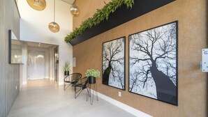 Een moderne hal met een houten accentmuur, twee grote gepresenteerde foto’s van kale bomen, een zithoekje met stoelen en een potplant, en hanglampen.