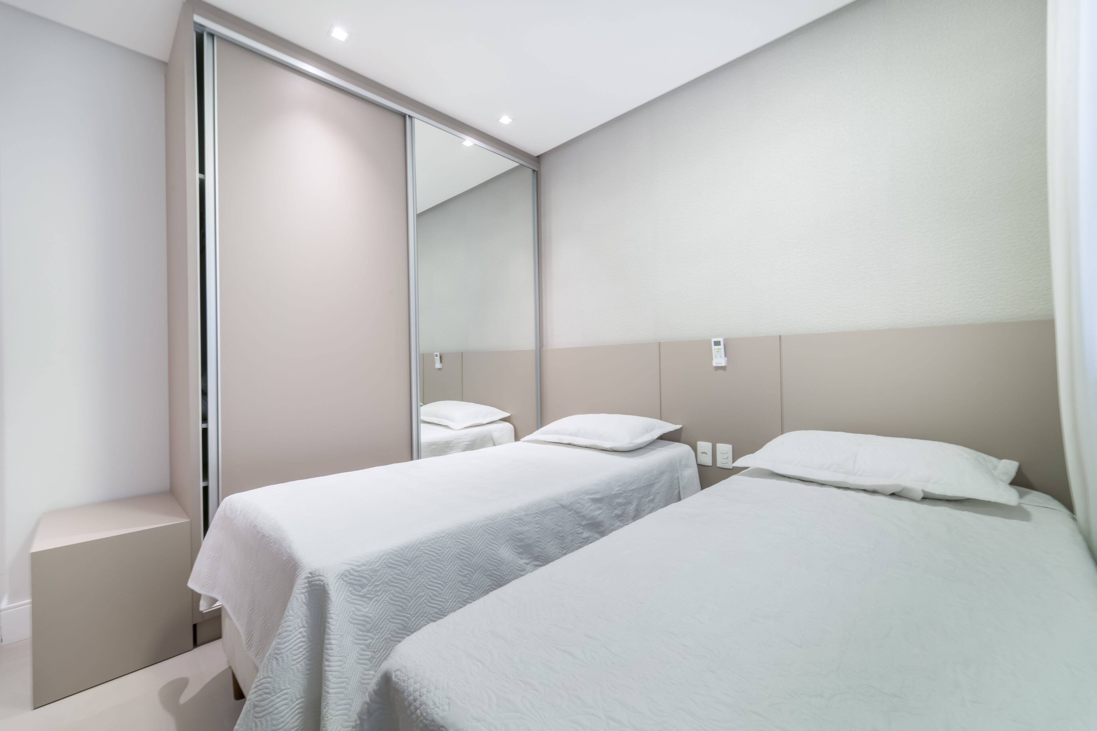 A modern hotel room with two single beds, a large mirror, and a sliding door closet.