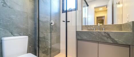 A modern bathroom with a glass-enclosed shower, a white toilet, and a marble countertop.