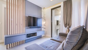 Een moderne woonkamer met een grijze bank, een flatscreen televisie bevestigd aan een grijze console, en een schuifdeur die leidt naar een balkon.