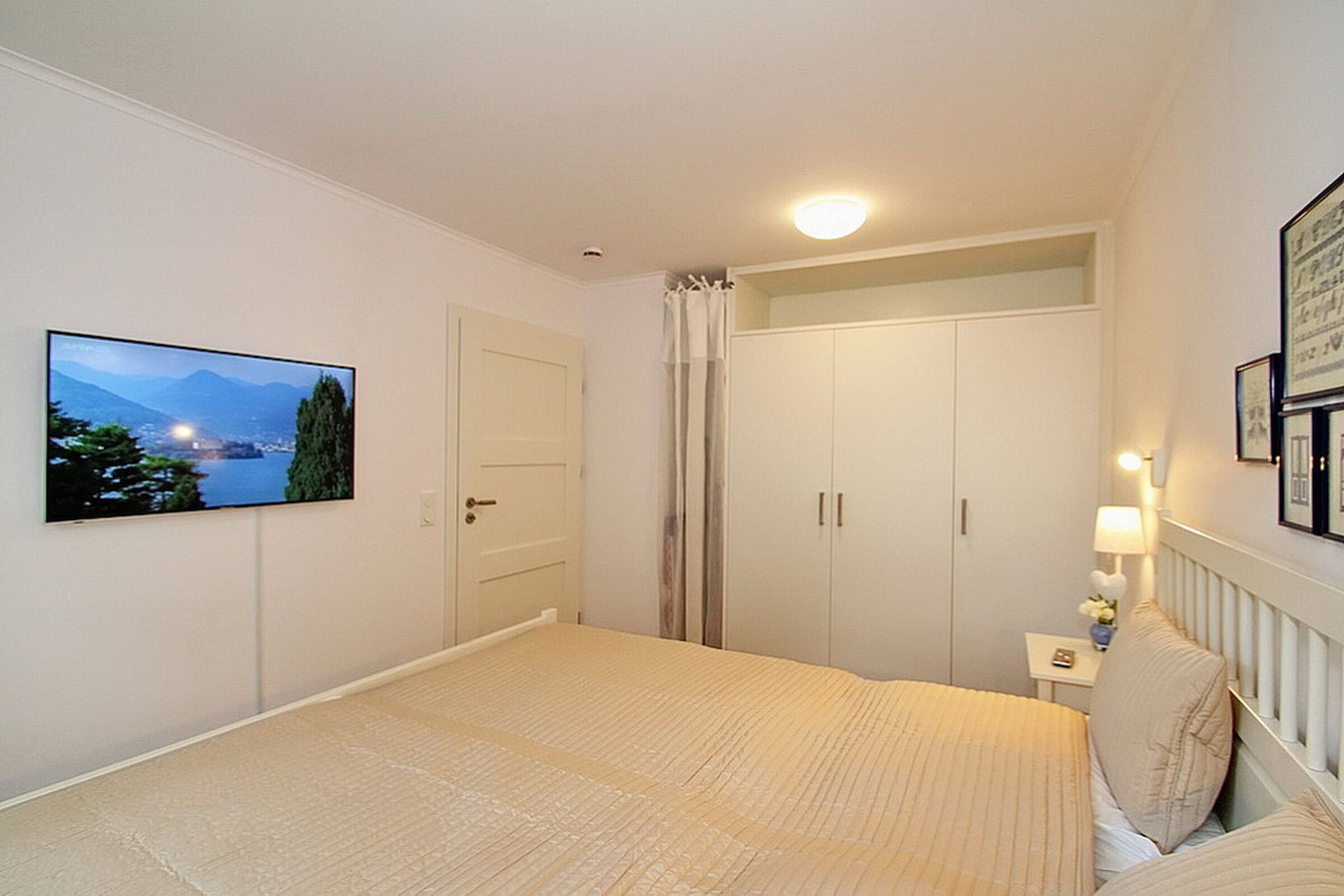 A bedroom with a bed, a nightstand, a lamp, a framed picture, and a door.