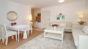 Una sala de estar moderna con un sofá blanco, una mesa de centro de vidrio y un comedor con sillas y mesa blancos.