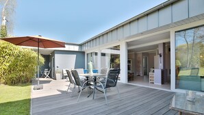 Un patio moderno al aire libre con una mesa y sillas de comedor, una sombrilla grande y vistas hacia la casa.
