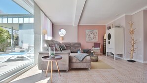 Una sala de estar moderna con un ventanal grande, un sofá gris, un espejo redondo y un mueble blanco.