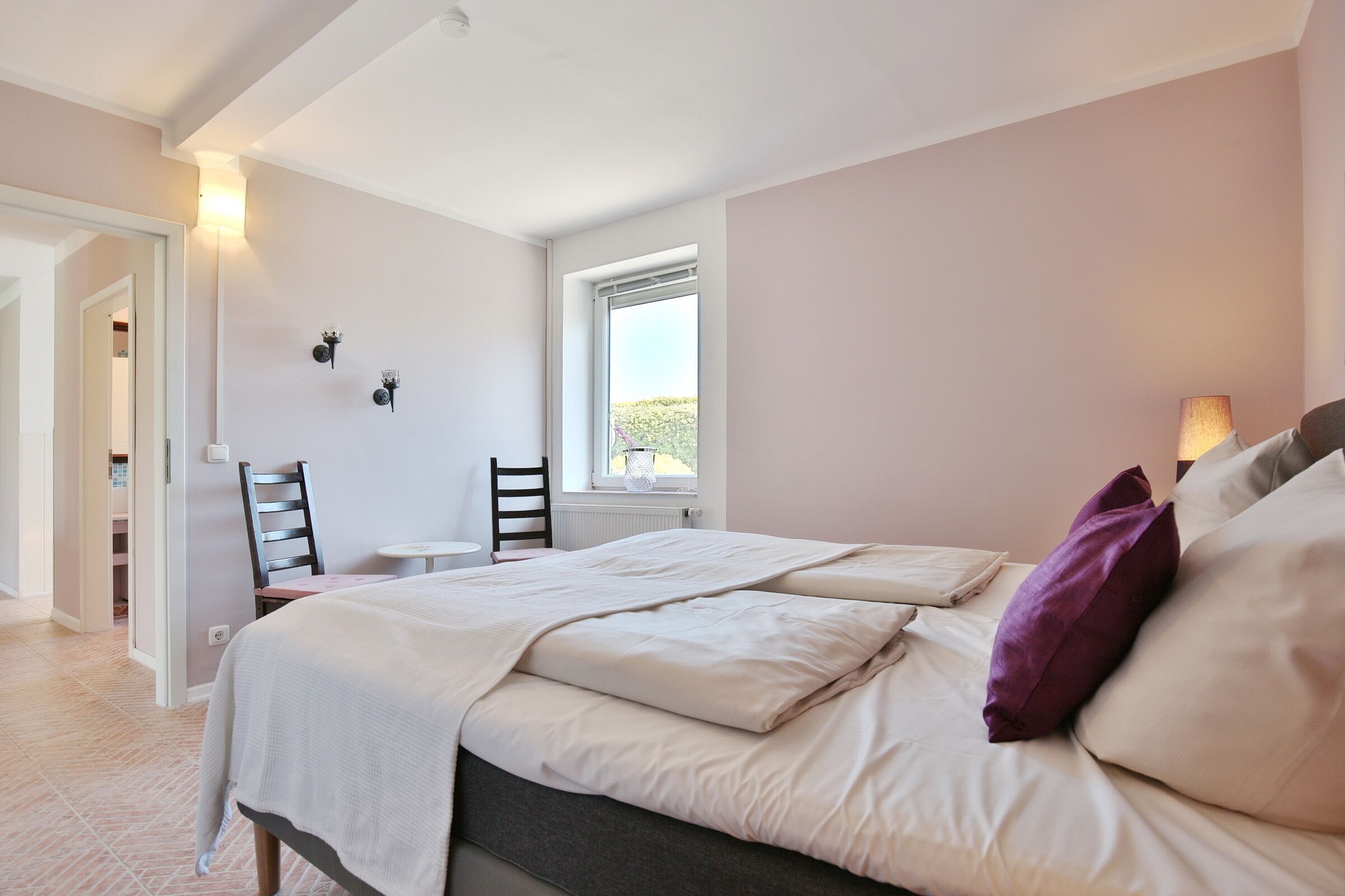 A bedroom with a bed, a chair, a small table, and a window.