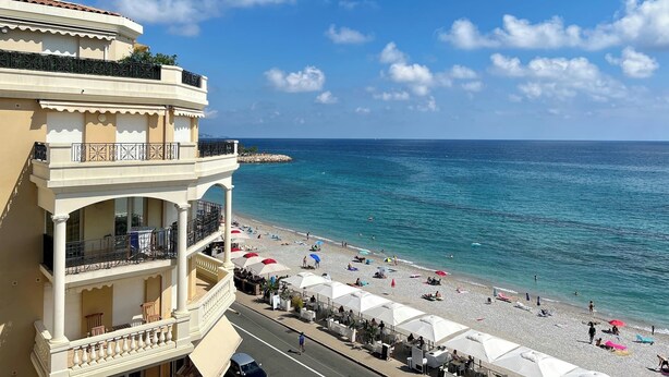 Un hôtel situé sur la côte, doté d’un balcon, offrant une vue sur la plage et disposant d’un espace extérieur aménagé pour s’asseoir.