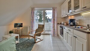 Une cuisine compacte avec un coin repas, un fauteuil à bascule et une vue dégagée sur l’extérieur grâce à une grande fenêtre.