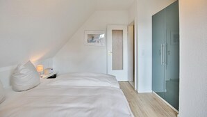 Une chambre à coucher avec un lit, une table de chevet avec une lampe, une porte et un tableau accroché au mur.