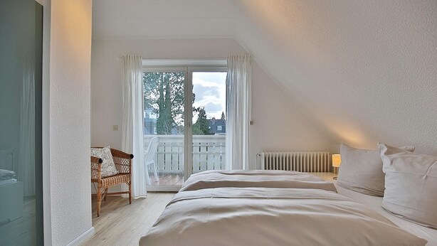 Une chambre avec un grand lit, une chaise et un balcon offrant une vue sur les arbres et les bâtiments.