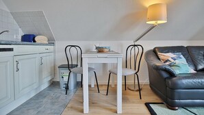 Een knus woongedeelte met een kitchenette, een eettafel met stoelen, een bank en een vloerlamp.