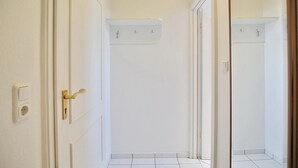 Een smalle gang met witte wanden, een betegelde vloer en een deur met een gouden handvat.