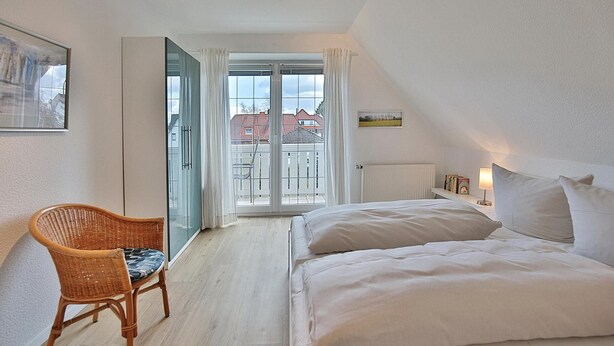 Een slaapkamer met een bed, een stoel, een raam en uitzicht op gebouwen.