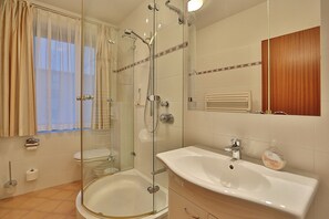 Ein modernes Badezimmer mit einer Duschkabine, einer freistehenden Badewanne, einem Waschbecken mit Spiegel und einer Toilette.