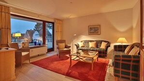 A living room with a large window, a sofa, a chair, a coffee table, and a lamp. - Haus Kastanienallee 3 Appartement 6 (Timmendorfer Strand)