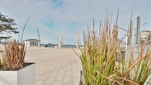 Un chemin pavé bordé de jardinières remplies de hautes graminées, avec une vue lointaine sur un pont.
