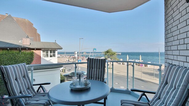 Un balcon avec une table et des chaises, donnant sur une plage et une jetée.