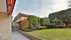 A modern building with a brick facade, a well-maintained lawn, and various shrubs and trees. - Haus Wolburgstrasse Appartement 23 (Timmendorfer Strand)