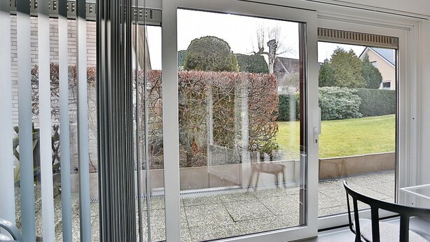 A room with a sliding glass door leading to a patio with a view of a garden and a house. - Haus Wolburgstrasse Appartement 23 (Timmendorfer Strand)