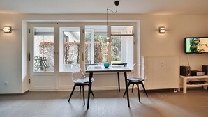 A dining area with a table and chairs, a pendant light, and a television on a stand. - Haus Wolburgstrasse Appartement 23 (Timmendorfer Strand)