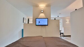 A bedroom with a bed, a mounted television, and a hallway leading to a bathroom. - Haus Wolburgstrasse Appartement 23 (Timmendorfer Strand)