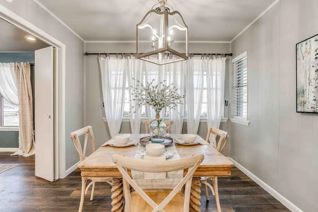 Un coin repas comprenant une table en bois, six chaises, un lustre et un vase avec des fleurs.